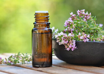 bottle of essential oil and lavender flowers on a table over green background