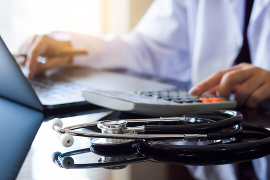 Doctor or physician using calculator and work on laptop computer with medical stethoscope on the desk at clinic or hospital. Medical healthcare costs ,fees and revenue concept.
