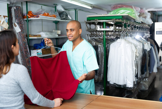 Smiling man drycleaner giving clean garments to client, satisfied with quality