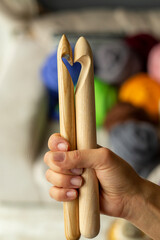 Two wooden knitting needles in a female hand on the background of multi-colored merino skeins in...