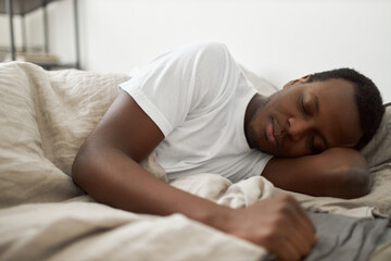 Fototapeta na wymiar People, bedding, bedtime, rest and relaxation concept. Indoor shot of handsome African American male wearing white t-shirt lying in bed, sleeping peacefully, having pleasant good dream