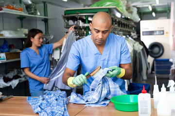 Confident man laundry worker cleaning shirt using brush at dry-cleaning facility
