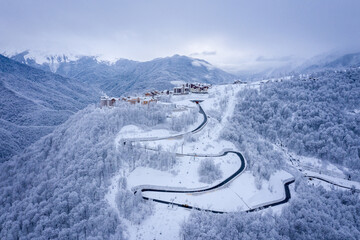 Winter aerial view of the Ski Resort Rosa Khutor and the mountain road to it. Beautiful winter landscape with frost-covered trees. Krasnaya Polyana, Sochi, Russia