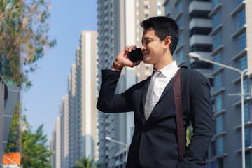 Asian businessman is standing and talking with his colleague in phone on the city streets during your morning commute..