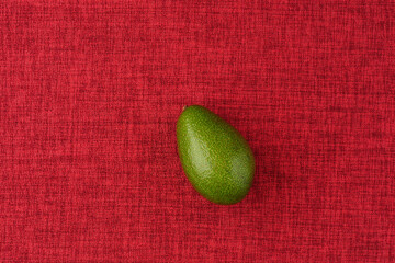 Avocado. A ripe green oval fruit on a red background