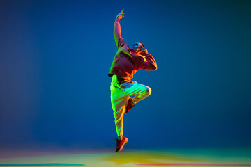 Young hip-hop dancer dancing isolated over blue background in neon light