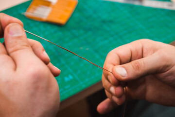 Hands sew a brown belt with threads and a needle