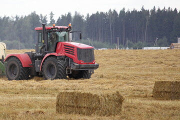 Modern red wheeled tractor on a harvested field on rectangular hay blocks background at autumn day, agricultural machinery in farming