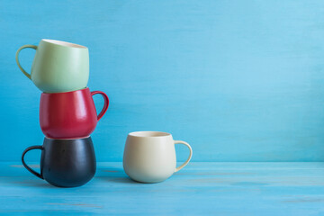 Colorful ceramic mugs on blue wooden background with copy space.