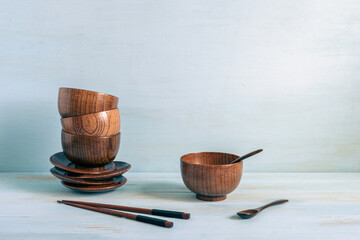 Miniature dark wooden bowls and plates, spoons and chopsticks for Asian meal over blue background with copy space.