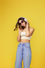 pretty young woman with headphones listening to music and dancing on yellow background.