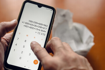 Male hands holding smartphone and counting monthly domestic bills, money accounting, home bookkeeping