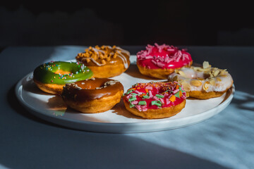 Obraz na płótnie Canvas Colorful Glazed Doughnuts with Sprinkles. Served on a White Plate