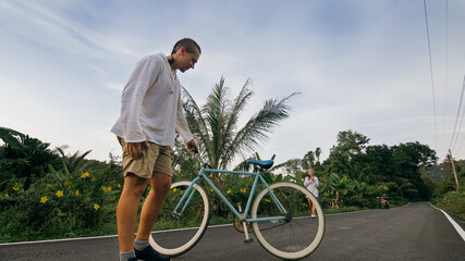 Naklejka premium Biking road trip. The man on blue bike in white clothes on forest road. The biker men ride on bicycle. Cycling Cycle Fix. Asia Thailand ride tourism. Take a photo with a bike.