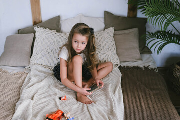 Obraz na płótnie Canvas little girl with long hair and bare feet playing phone on the bed