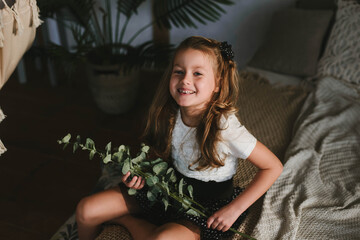 little girl in a white t-shirt with a green sprig of eucalyptus in her hands