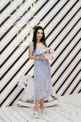 slender brunette in a blue dress stands with a bouquet of flowers