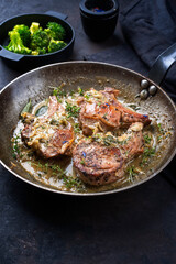 Traditionelle gegrillte dry aged Koteletts vom Kalb mit Kräuter und Brokkoli in Butter Jus serviert als close-up in einer rustikalen Eisenpfanne 