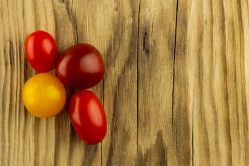 Small colorful tomatoes stacked on a wooden chopping board. Artificial light from two lamps, soft shadows