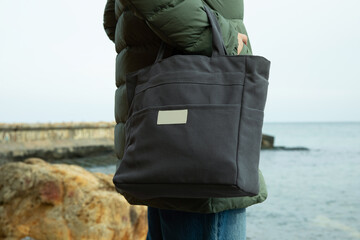 Woman in winter clothing with stylish eco bag on sea shore
