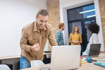 Obraz premium Fair-haired bearded young man looking at the laptop and feeling happy