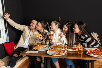 groups of young people take a selfie photo while eating pizzas at a restaurant