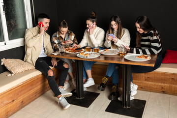 a group of young people are using their cell phones in a pizzeria
