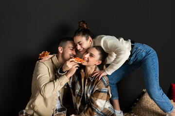 two girls and a boy are joking while eating a slice of pizza.