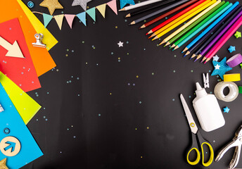 Bright colorful background with colored pencils, paper, scissors, glue for children's creativity on a black table. Space to copy.
