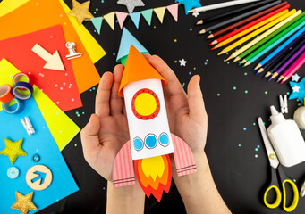 Step-by-step instruction crafts with children from rolls of toilet paper on the theme of space and rocket. Step 7 Craft space rocket made of colored paper in children's hands.