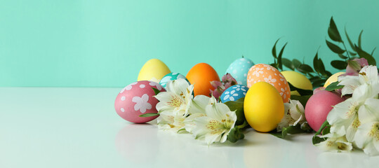 Color Easter eggs and alstroemeria flowers against mint background