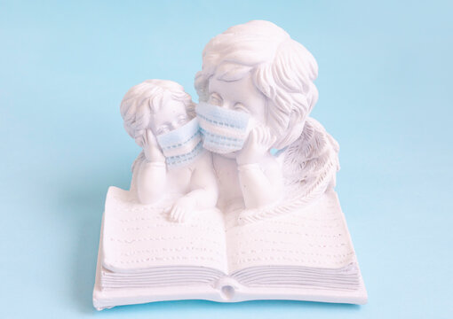 Angels Mom And Baby Bent Over A Book In Face Protective Mask On A Blue Background, The Concept Of Education And Motherhood