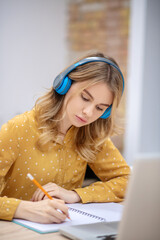 Blonde pretty girl in earphones sitting at the table and listening carefully