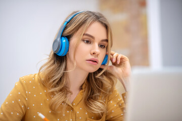 Blonde pretty girl in earphones sitting at the table and listening carefully