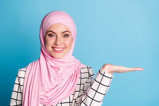 Close-up portrait of pretty cheerful content muslimah girl holding on palm copy space advice isolated over bright blue color background