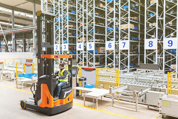 Storehouse employee in uniform working on forklift in modern automatic warehouse. Boxes are on the shelves of the warehouse. Warehousing, machinery concept. Logistics in stock. © Алина Бузунова