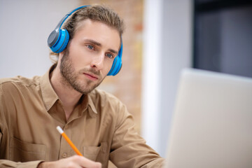 Young bearded guy in earphones sitting at the table and listening carefully
