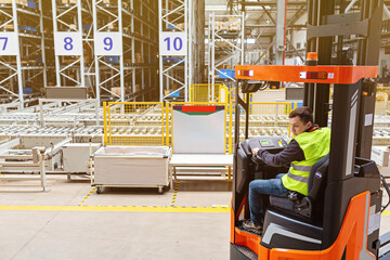 Storehouse employee in uniform working on forklift in modern automatic warehouse. Boxes are on the shelves of the warehouse. Warehousing, machinery concept. Logistics in stock. © Алина Бузунова