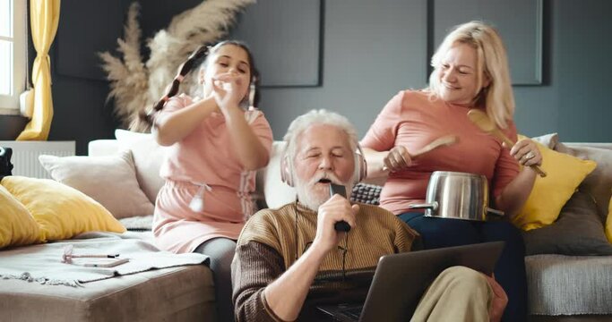 Funny grandfather with pink headphones sings to his granddaughter at home. Family fun and laughter. Family fun concept.