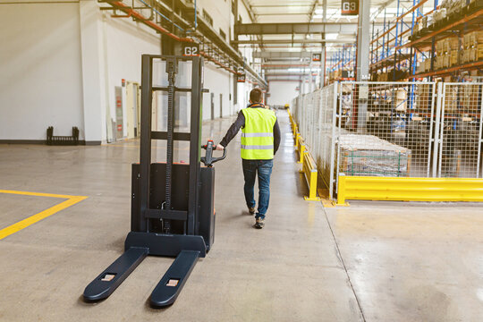 Storehouse employee in uniform working on forklift in modern automatic warehouse. Boxes are on the shelves of the warehouse. Warehousing, machinery concept. Logistics in stock.