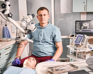 Young male dentist sitting bedside patient in dental office.