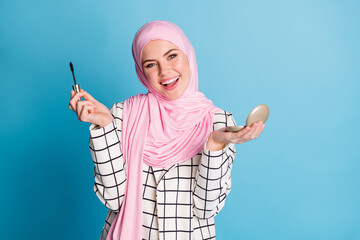 Portrait of pretty cheerful muslimah girl holding in hands mirror mascara preparing isolated over...