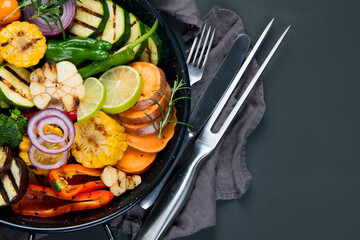 Grilled assorted vegetables in cast iron pan on black background.