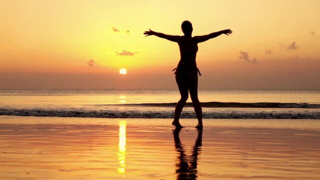 Young, happy woman turning on the beach at sunset super slow motion 
