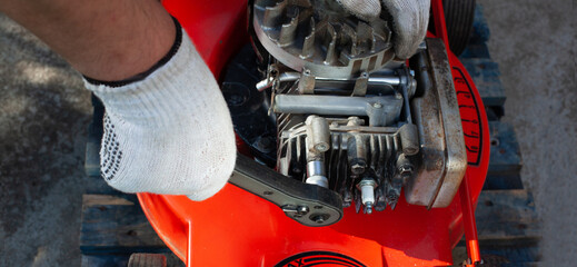 Repairman fixes the lawn mower engine with tools at the workshop. - obrazy, fototapety, plakaty