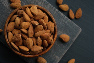 Almonds nuts close-up in a round wooden cup on a black shabby chic board on a black schiffer blurred background.Nuts and seeds. .Healthy fats.Heap Almonds shelled  nut closeup. organic snack 