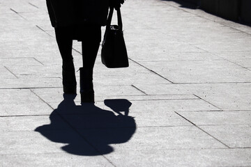 Black silhouette and shadow of lonely woman with handbag walking on a street. Concept of female fashion and footwear