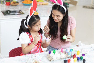 Attractive young woman with little cute girl are preparing for Easter celebration. Mom and daughter wearing bunny ears are spending time together before Easter while painting eggs.