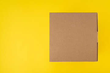 Unprinted cardboard box on yellow background top view. Copy space. Mock up.