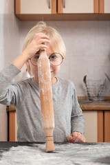 Child in kitchen with wooden rolling pin is about to cook cookies.